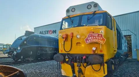 Alstom Two historic trains in the Alstom rail yard in Derby. One train is yellow with a sign that says 'The Greatest Gathering' on the front.