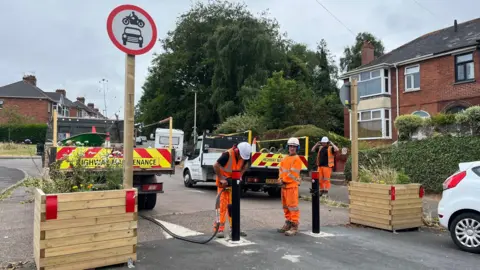 Workmen removing a bollard on Hamlin Road in Exeter between two wooden planters