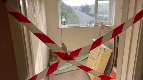 Simon Thake Red and white tape is crossed over a bedroom doorway. Inside cabinets and boards are piled up