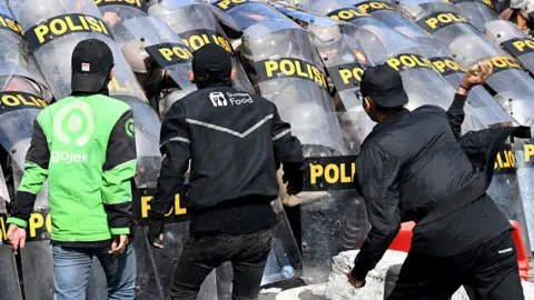 Getty Images Protesters clash with police who hold up riot shields during a protest in front of a police station in Denpasar, Bali, Indonesia