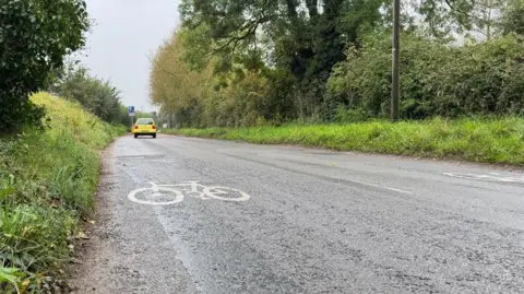 A car is driving away from the camera. There is a bicycle sign in the road. It's an overcast day.