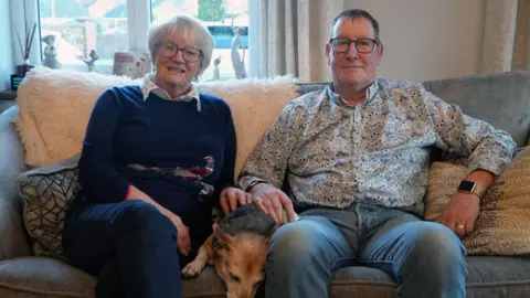 Margaret and Tim Metcalfe sat on a sofa with a dog