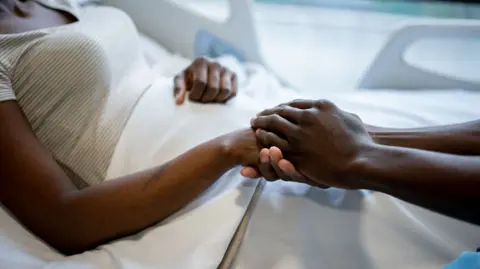 stock image of someone reaching towards a hospital bed and holding the hand of a patient 