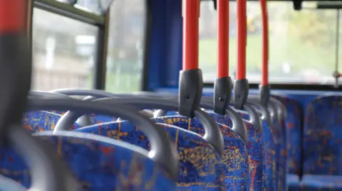 Blue-patterned bus seats with grey and orange hand rails sticking out of the top of them