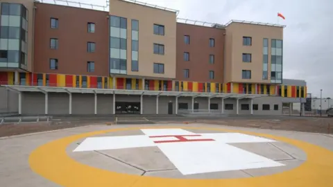 A multi-storey building with a large helicopter landing pad in the foreground