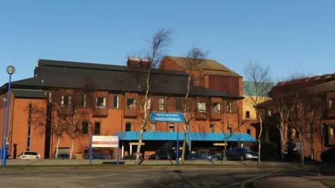 Anna Gowthorpe/PA Media Image shows the front of Scarborough Hospital. You can see a red brick building with a sign saying 'Main entrance', with trees and a car park in front of the building