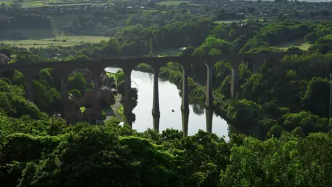 Getty Images Long bridge over a river surrounded by green trees and fields