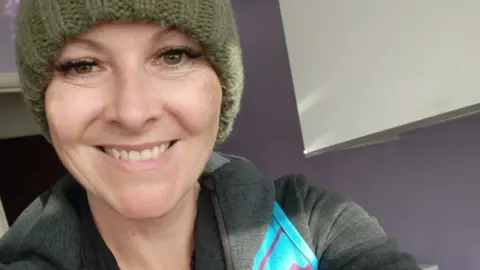 Stevie O'Brien A smiling woman in a beanie hat and grey hoodie.