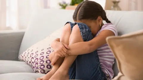 A girl sitting on a white sofa with her knees up 