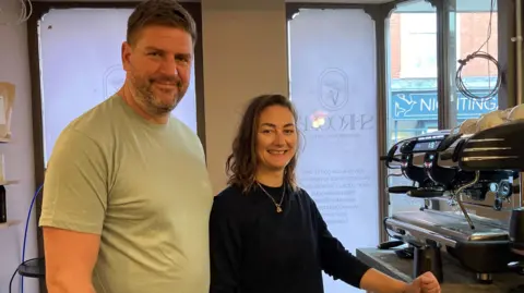 Paul and Alex Murray stand in front of a coffee machine. Shrooma (the name of the cafe) is written behind them on the shop window.  