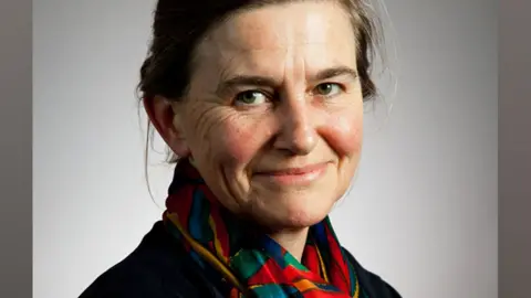 Graham Copekoga Prof Amy Erickson wearing a brightly coloured scarf and dark top looking towards the camera