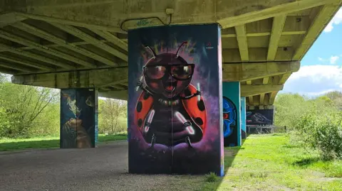 Tony Nero Mural of a beetle insect, smiling with some other artworks on pillars in the background can be seen.