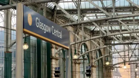 A blue sign with a yellow stripe at the bottom for 'Glasgow Central' inside of the station.