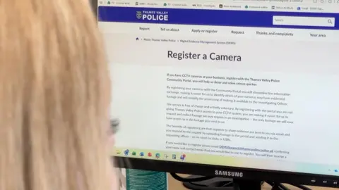 A woman with blonde hair looking at a computer screen, with the page 'register a camera' on Thames Valley Police's website on the screen