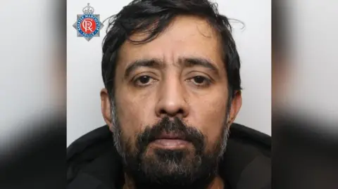 Mugshot of Daniel Hashmi. He has dark hair and a beard, and wears a dark coat.