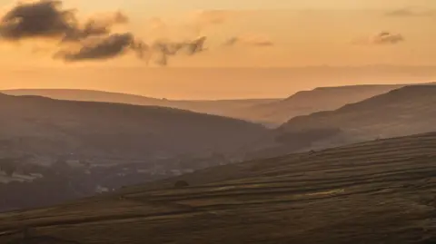 PA Media A view over hills and fields, with a yellow sky and slight mist in the distance