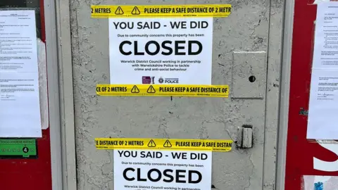 Warwick District Council The front door of a shop has been painted over in grey. It is covered in yellow tape urging people to keep a safe distance. Two notices on the front say 'You said, we did, closed" in large letters.