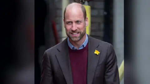 Getty Images Prince William wearing a black jacket with a daffodil on the left lapel, he has a maroon jumper underneath a blue shirt under that 