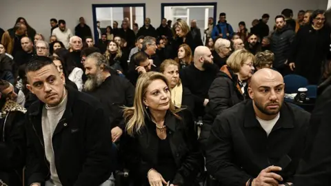 Former Tempi 2023 Victims' Association president Maria Karystianou sits with relatives inside the "Gaipolis" conference venue at the University campus in Larissa
