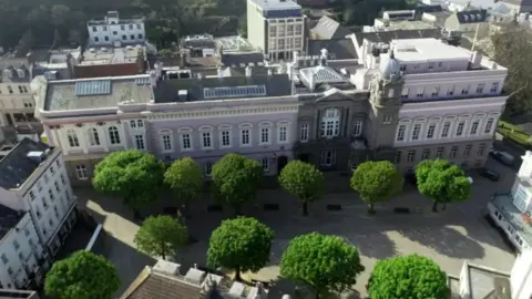 An aerial view of buildings surrounded a walkway area with two rows of trees surrounding it.