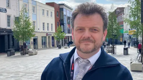 A head and shoulders picture of Sergeant Christian Denning from Essex Police in a pedestrianised area of Chelmsford city centre