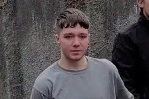 A 20-year-old man wearing prison clothes being escorted from court by a security guard