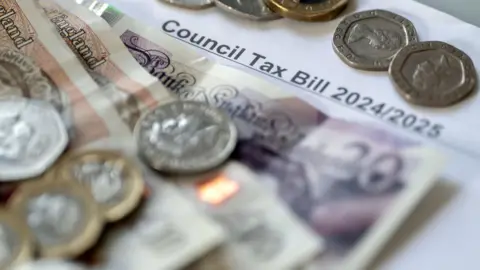 Two £10 notes and a £20 note are stacked up on top of a council tax bill, along with a handful of coins.