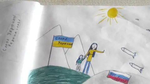 Olga Podolskaya Um desenho de Masha, de 12 anos, parece mostrar uma mulher ucraniana com uma criança levantando a mão para dizer não enquanto mísseis russos se aproximam