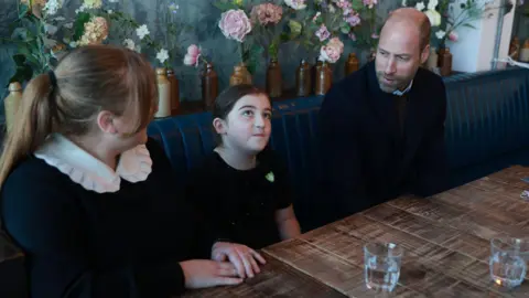 PA Media Prince William sat in a pub talking to two young girls