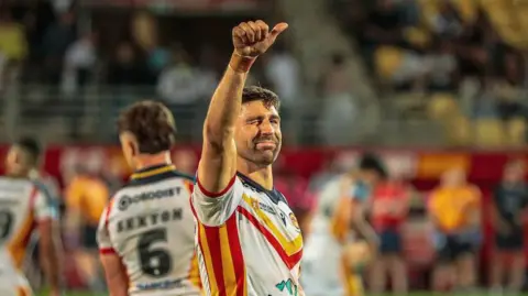 Catalans Dragons winger Tommy Makinson celebrating by raising his right thumb up and winking towards the crowd.
