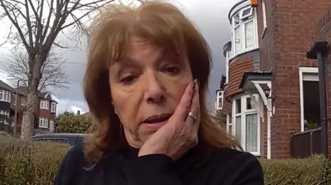 Greater Manchester Police Daryl Berman with brown shoulder length hair with her hand to her face standing outside her home as she spoke to police officers captured on police body worn cameras. 