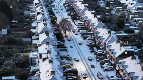 Aerial view of snow-covered rooftops of houses lining a road, also covered in snow