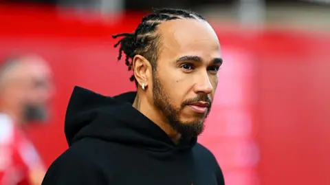Getty Images Dressed in a black hoodie, F1 driver Lewis Hamilton walks in the Paddock ahead of a race