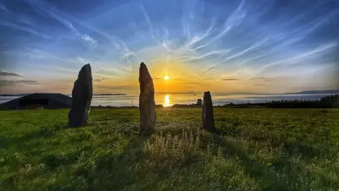 The Ballochroy standing stones in Kintyre in front of a sunset over water