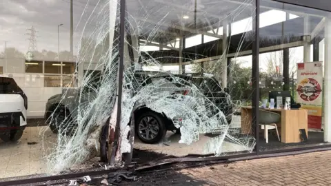 A car showroom with smashed windows and oil on the floor at the scene of the crash. 