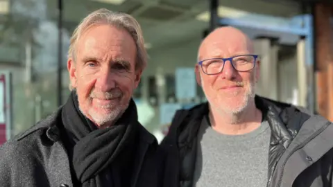 Mike Rutherford and another resident standing outside Chichester District Council offices both wearing winter jackets looking at the camera