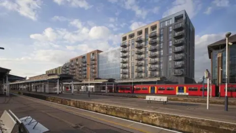 The new flats standing over Guildford station with a red South Western Railway train at the platform