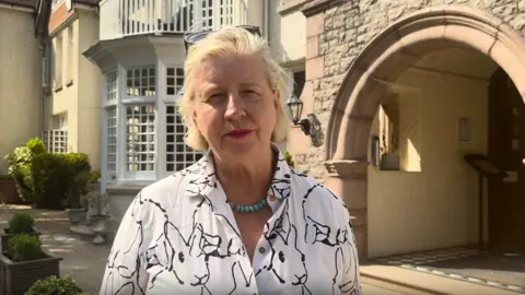 Constable Karen Shenton Stone has cropped blonde hair and is pictured outside Chateau La Chaire. She is wearing a white shirt and has sunglasses on her head. She has a serious expression. 