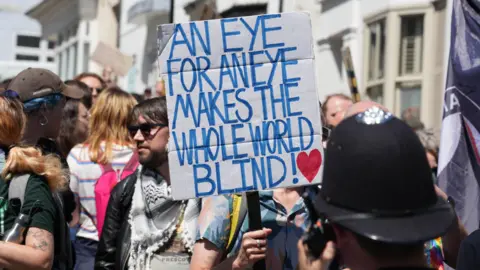 Eddie Mitchell A person holding a sign which reads "an eye for an eye makes the world blind".