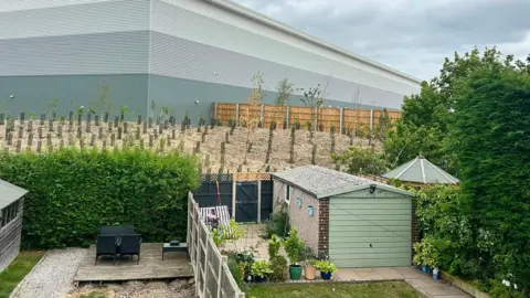 Amanda Robinson A large warehouse looms over a garden view 