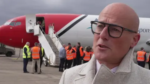 Christian Foster, Doncaster Sheffield Airport's programme director, standing in front of crew in hi-vis jackets and a Boeing 727 plane.