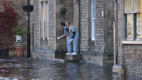 Two dental assistants in grey uniform standing on a step outside the practice, surrounded by floodwater