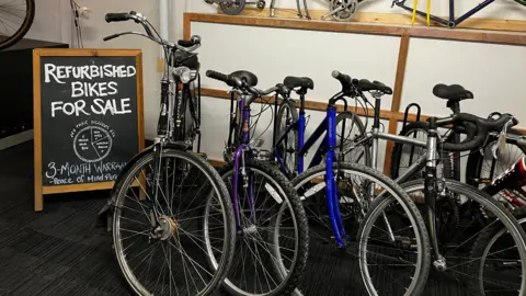 Five bikes lined up next to an A-board that says Refurbished Bike For Sale