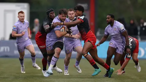 Will Trenholm (centre) charges through a tackle as Noah Caluori puts his arm on his shoulder and Maro Itoje (second left) grabs him from behind
