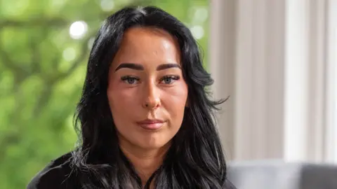 Kiera looks straight at the camera in a close-up shot. She has dark long hair