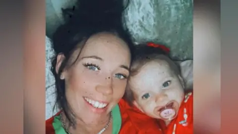 Kerry Blackaller, a woman with black hair, lies down with her daughter. They have matching red tops on.