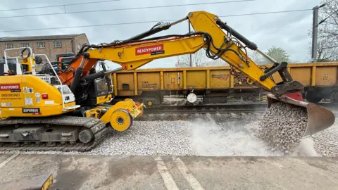 A yellow digger at the site of a level crossing where maintenance work is being carried out.