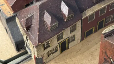 A miniature model of a house. The house is white and has multiple windows.