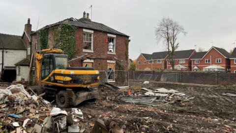 A derelict house with a digger in the foreground