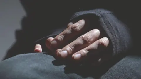 A close-up picture of some hands, folded in someone's lap. The person is wearing a long-sleeved black top and the sleeves are covering the back of their hands. 